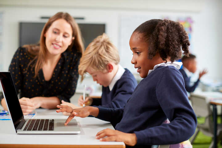 teacher and primary school children working at laptops