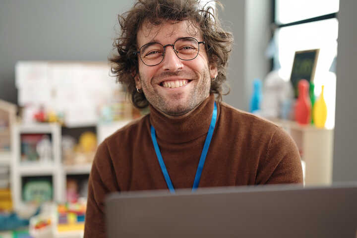 teacher with glasses and a lanyard using a laptop